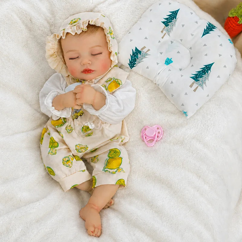 A realistic sleeping reborn baby doll wearing a cream ruffled bonnet and lemon-print romper lies on a soft white blanket, with hands clasped, a pink pacifier nearby, and a tree-patterned baby pillow beside it.