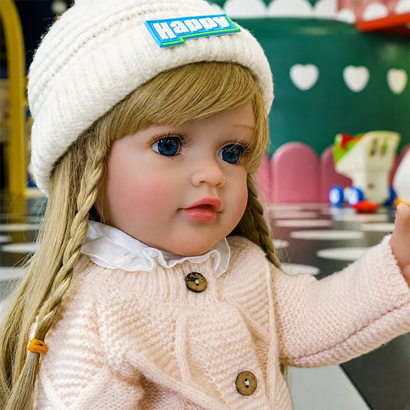 Fashionable reborn girl doll dressed in a textured pink cardigan, layered white tulle skirt, cozy knit hat, and white shoes.