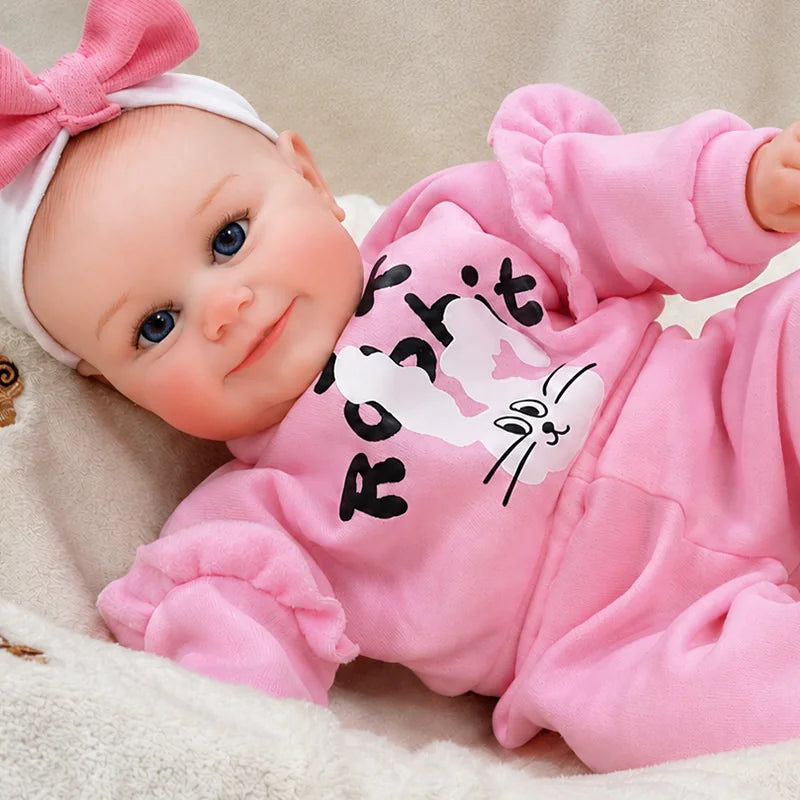 Adorable reborn baby doll relaxing in a cozy nursery setting, wearing a bright pink outfit and bow while smiling sweetly at the camera.