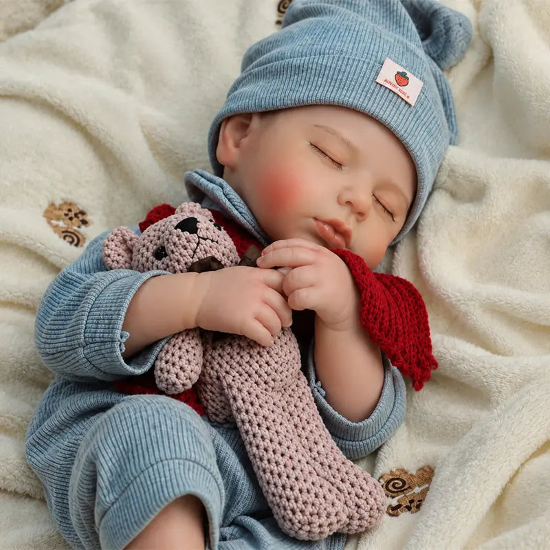Sleeping Reborn Baby Doll with lifelike closed-eye expression, soft blue outfit and cozy red scarf.