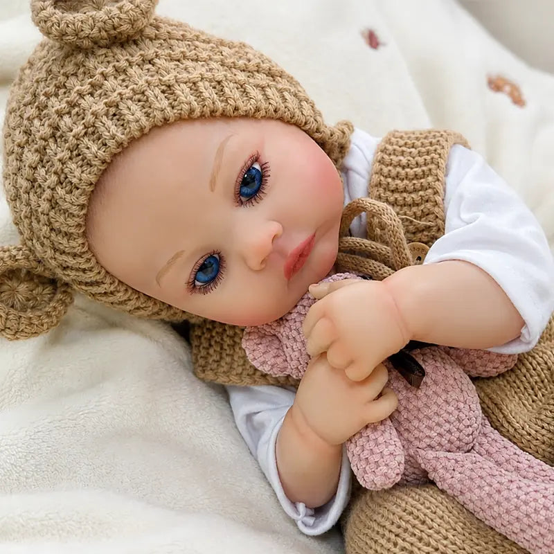 Cozy reborn baby doll resting with a pink teddy bear, ideal for nursery displays, pretend play, cuddling, and gift-giving.