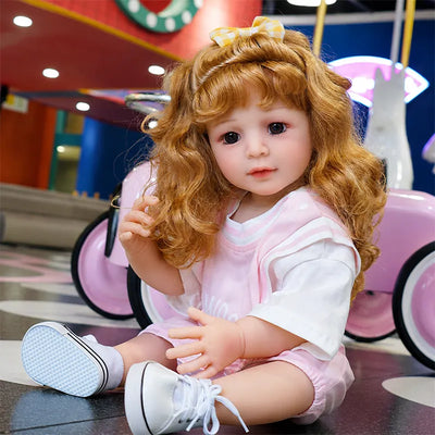 Lifelike reborn toddler doll with realistic facial details, expressive brown eyes, curly auburn hair, and a charming pink outfit.