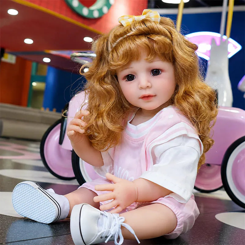Lifelike reborn toddler doll with realistic facial details, expressive brown eyes, curly auburn hair, and a charming pink outfit.
