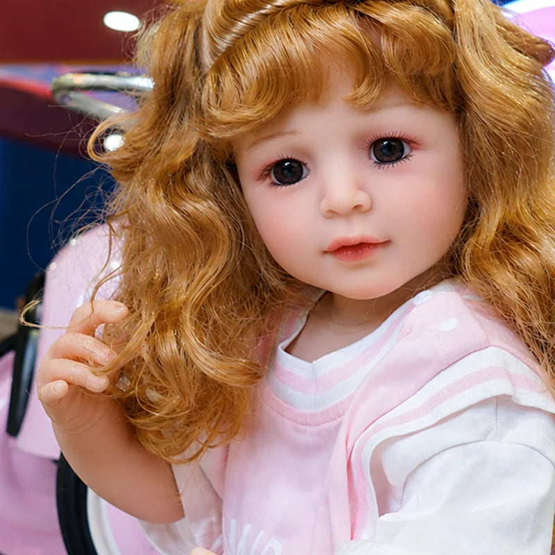 Reborn toddler doll featuring delicate eyelashes, rosy cheeks, softly painted lips, detailed fingers, and naturally styled curly hair.