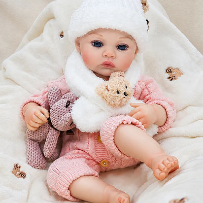 Lifelike reborn baby girl relaxing in a cozy blanket setting, dressed in a pink knit romper with charming winter accessories.