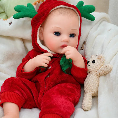 Bright-eyed reborn baby doll wearing a plush red reindeer suit with green antlers and holding two festive toys.