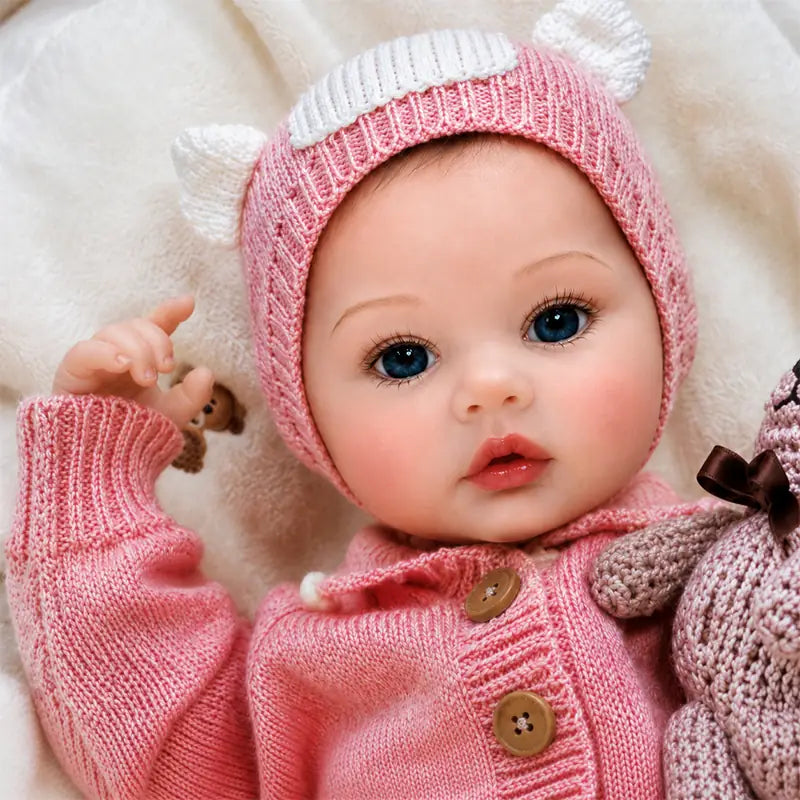 Close-up of a reborn baby girl doll featuring glossy blue eyes, softly blushed cheeks, natural pink lips, and detailed fingers.