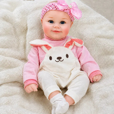 Cute reborn baby girl wearing cream bunny overalls, a pink long-sleeve top, and white knitted socks.
