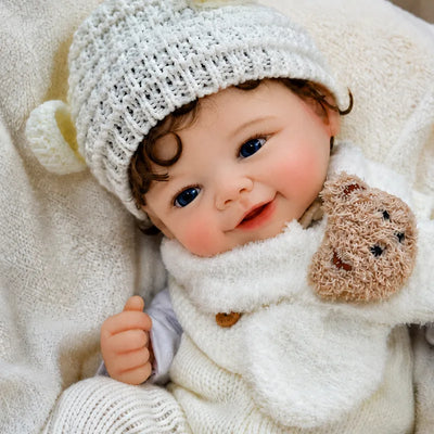 Smiling Full Silicone Reborn Baby Doll dressed in a cream knitted outfit, animal-ear hat, and teddy bear scarf.