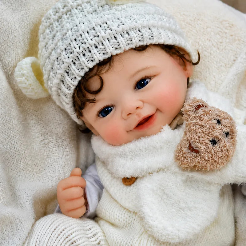 Smiling Full Silicone Reborn Baby Doll dressed in a cream knitted outfit, animal-ear hat, and teddy bear scarf.