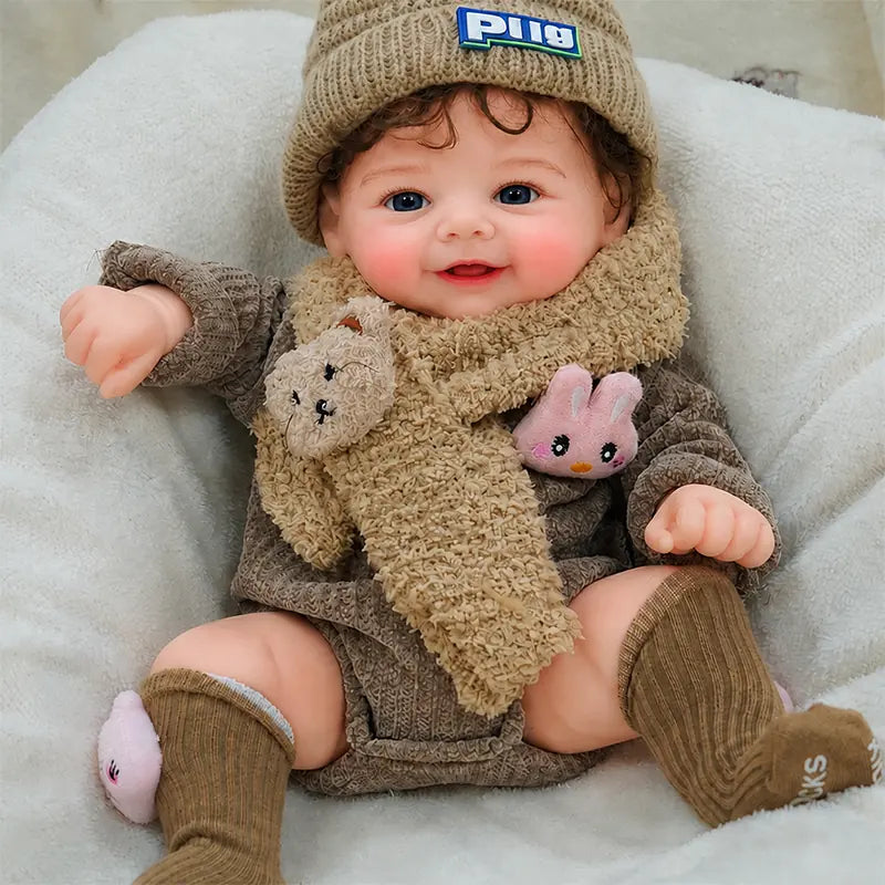 Realistic smiling silicone reborn baby doll wearing a brown knitted hat and cozy outfit, cuddling a plush teddy bear on a soft white blanket.