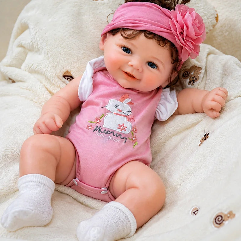 Full Silicone Reborn Baby Doll with a cheerful open-mouth smile, blue eyes, a pink floral headband, and a bunny romper. 
