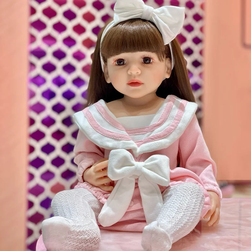 Interactive toddler doll with silky brown hair, straight bangs, a large white bow, pink sailor-style clothing, and knit tights.