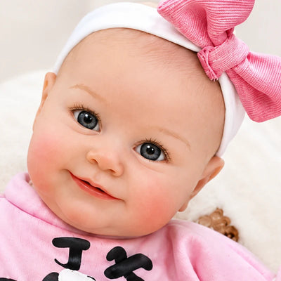 Smiling reborn baby girl doll with open eyes, chubby hands and feet, rosy cheeks, and a playful pink rabbit-themed outfit.