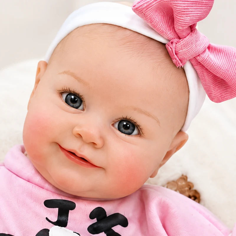 Smiling reborn baby girl doll with open eyes, chubby hands and feet, rosy cheeks, and a playful pink rabbit-themed outfit.