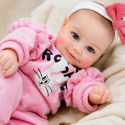 Lifelike reborn baby doll with bright blue eyes, rosy cheeks, a gentle smile, and an adorable pink bunny outfit.