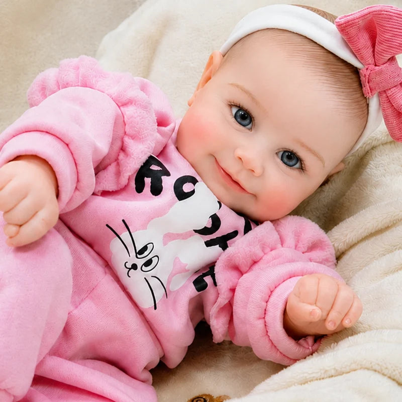 Lifelike reborn baby doll with bright blue eyes, rosy cheeks, a gentle smile, and an adorable pink bunny outfit.