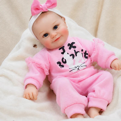 Realistic reborn baby doll dressed in a pink bunny tracksuit with ruffled sleeves and a matching bow headband.
