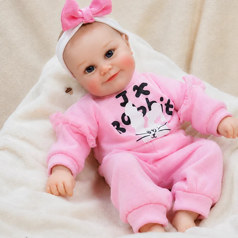 Realistic reborn baby doll dressed in a pink bunny tracksuit with ruffled sleeves and a matching bow headband.