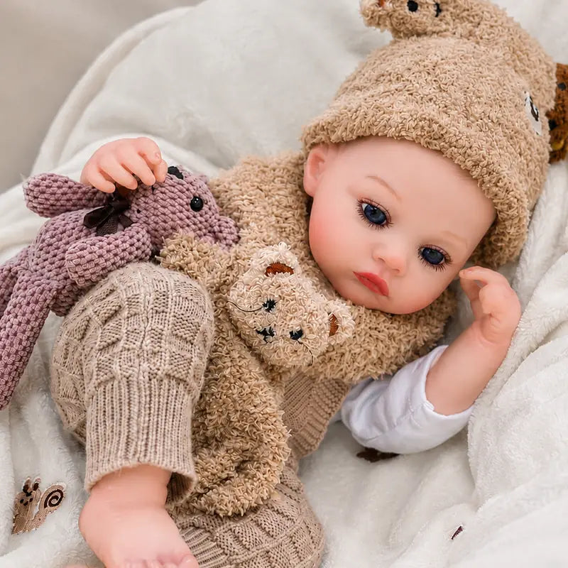Lifelike reborn baby doll with bright blue eyes, realistic facial details, and an adorable teddy bear outfit.