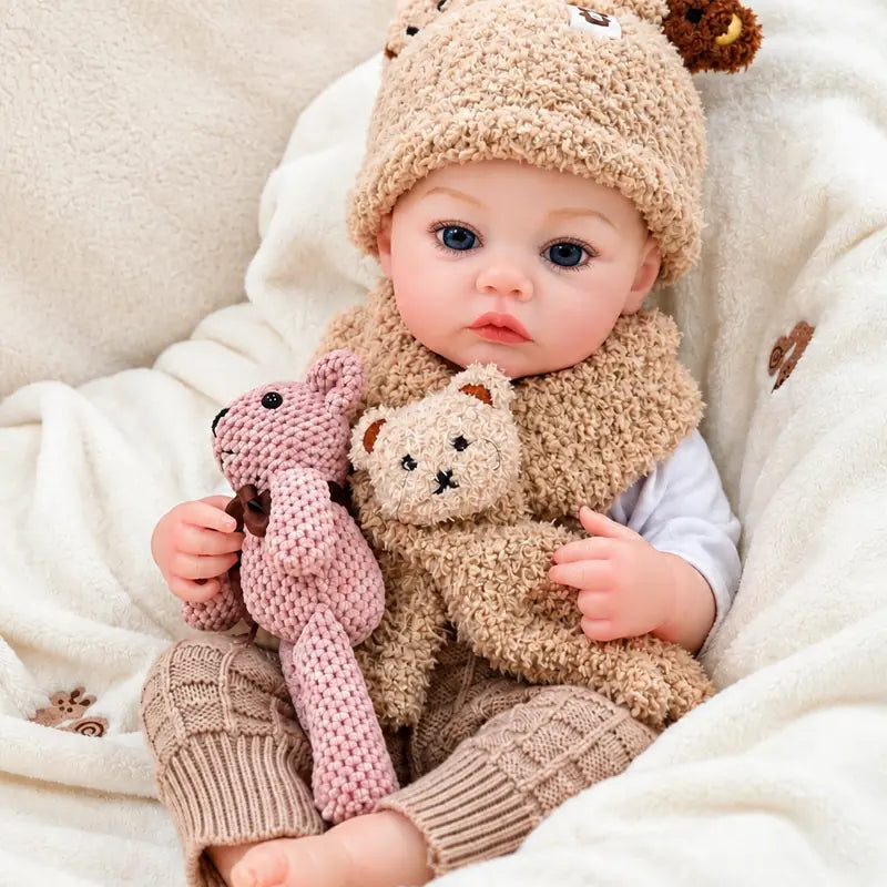 Realistic reborn baby doll sitting in a cozy nursery chair with a pink knitted bunny, ideal for pretend play and display.