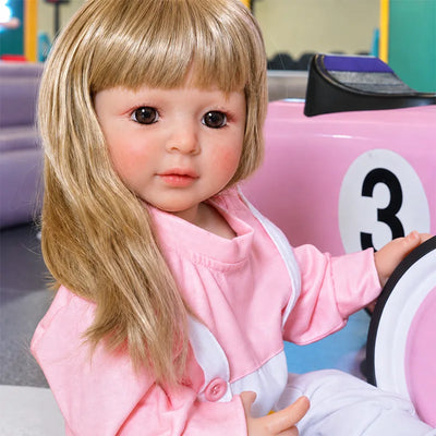Blonde reborn girl doll wearing a pink long-sleeve shirt, white overalls, white socks, and sporty sneakers.