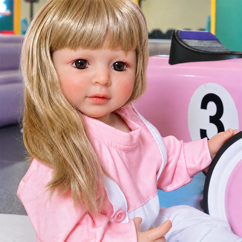 Blonde reborn girl doll wearing a pink long-sleeve shirt, white overalls, white socks, and sporty sneakers.