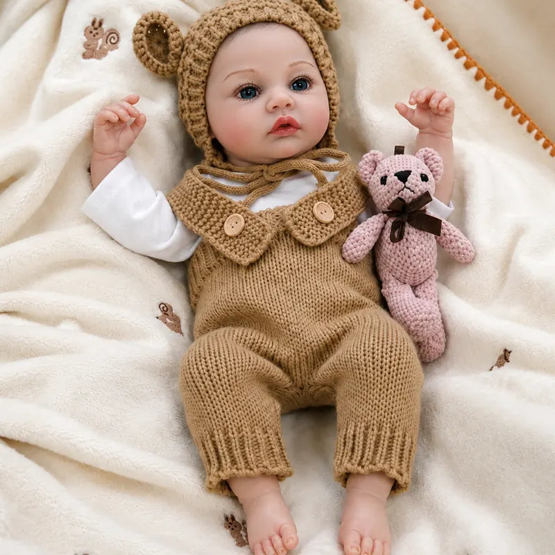 Little Honey lifelike reborn baby doll wearing a brown knitted bear outfit and lying on a soft cream nursery blanket.