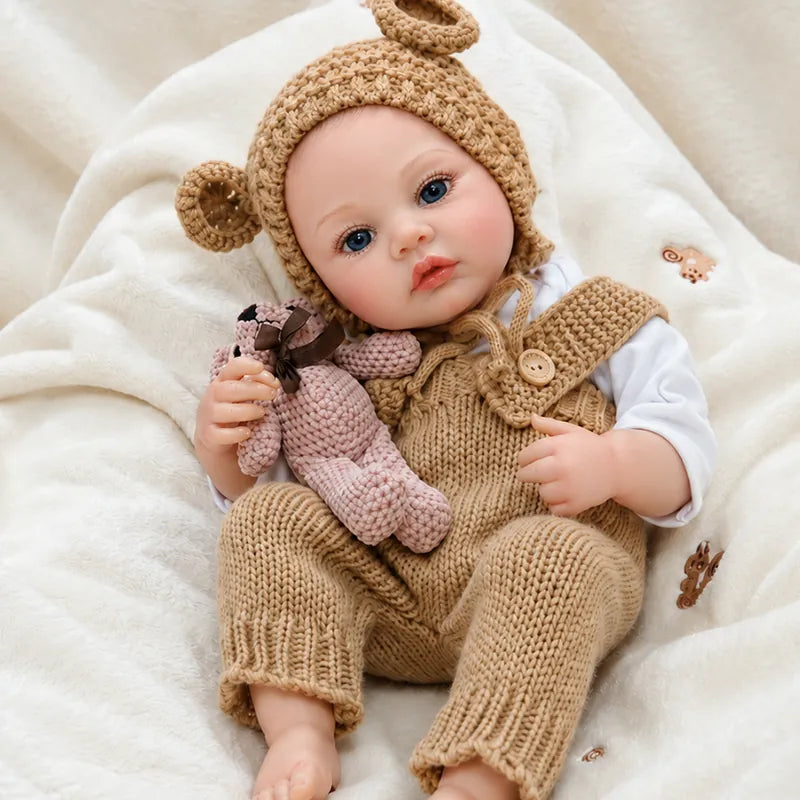 Artfully crafted reborn baby doll featuring layered skin painting, detailed facial coloring, and a textured hand-knit bear outfit.