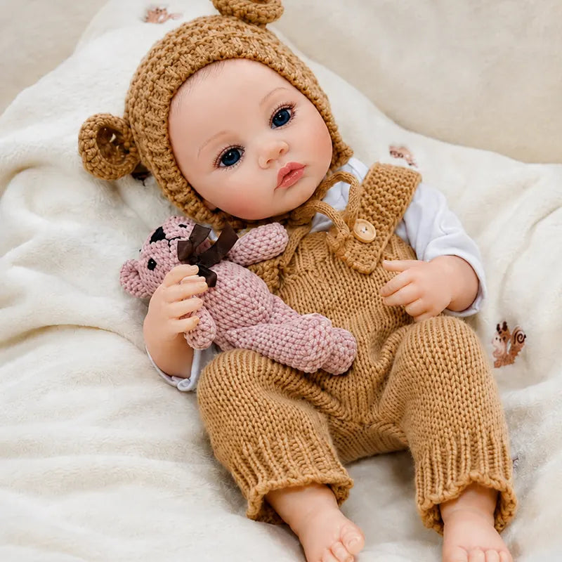 Lifelike baby doll enjoying a cozy morning on a plush blanket with her favorite pink teddy bear beside her.