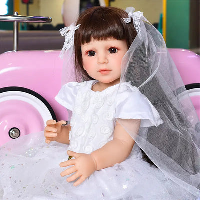 Blue-eyed reborn girl doll wearing a sparkling white floral gown, lace veil, and matching hair bows.